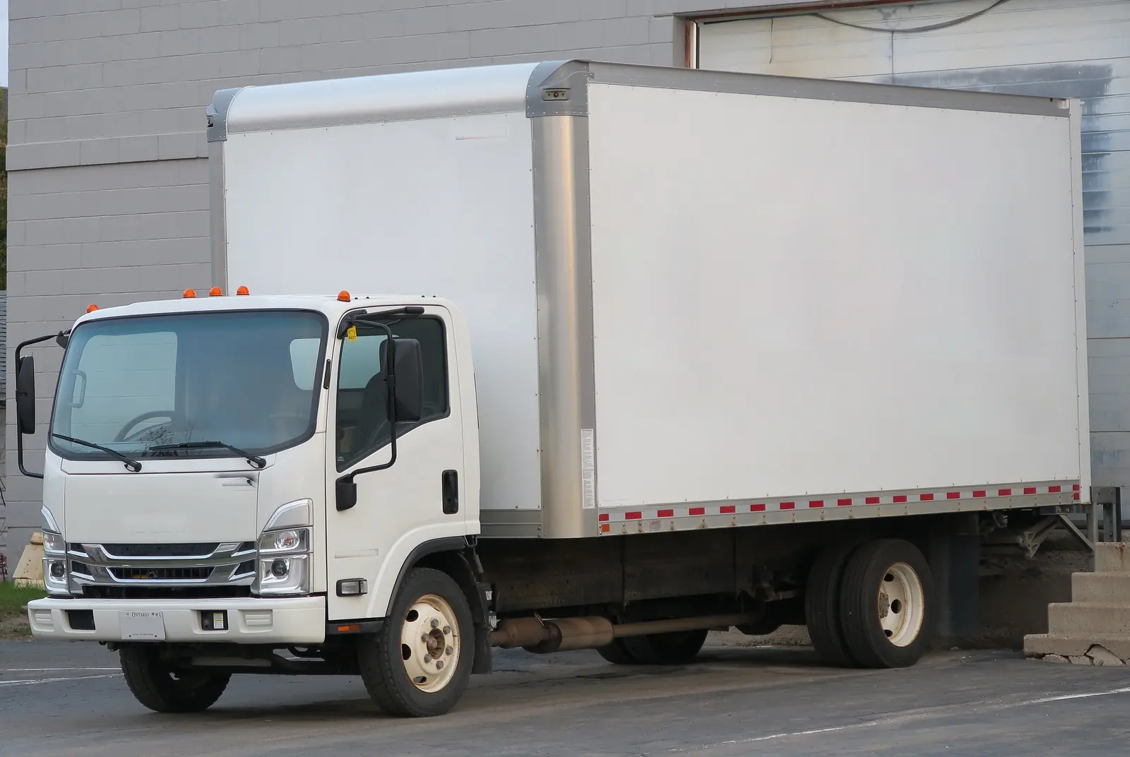 A white straight box truck parked beside a building, the kind of vehicle used for smaller expedited loads
