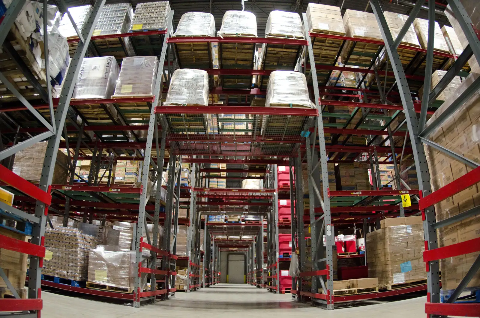 Aisle of a distribution warehouse with high racking full of shrink-wrapped pallets of packaged goods